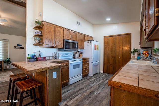 kitchen featuring sink, white appliances, a breakfast bar area, dark hardwood / wood-style flooring, and tile countertops