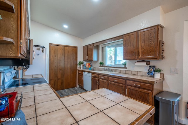 kitchen with sink, white appliances, tile counters, and vaulted ceiling