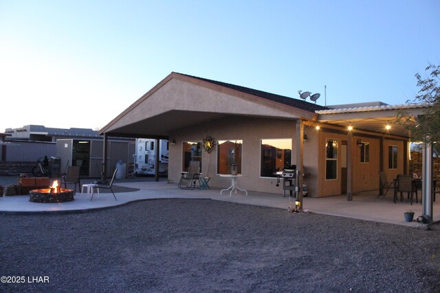 back of house at dusk with a fire pit, a patio area, and stucco siding