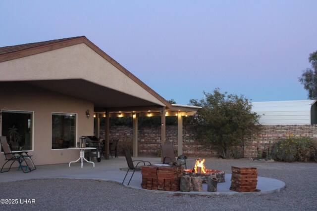 patio terrace at dusk featuring a fire pit and grilling area