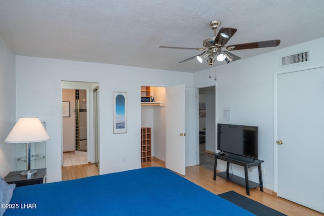 bedroom featuring a spacious closet, a textured ceiling, ensuite bathroom, light hardwood / wood-style floors, and ceiling fan