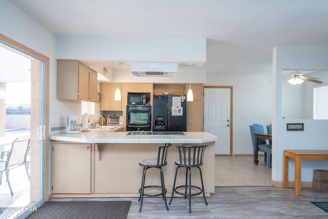 kitchen featuring pendant lighting, tile counters, black appliances, and kitchen peninsula