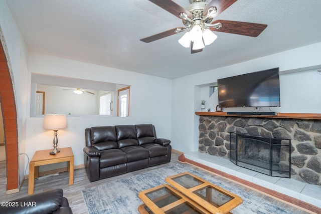 living room with a stone fireplace, wood-type flooring, and a textured ceiling