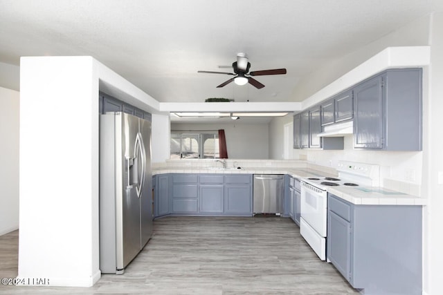 kitchen with tile countertops, sink, ceiling fan, light hardwood / wood-style floors, and stainless steel appliances