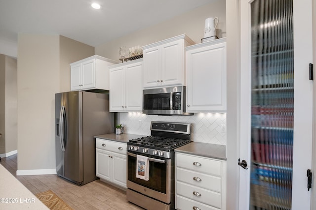 kitchen with baseboards, light wood-style flooring, backsplash, white cabinets, and stainless steel appliances