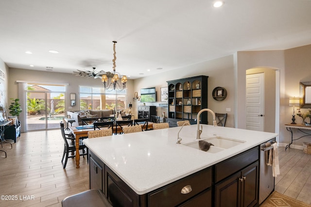 kitchen with stainless steel dishwasher, light wood-style flooring, a kitchen island with sink, a sink, and open floor plan