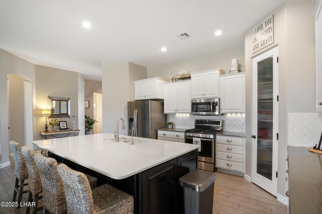 kitchen with visible vents, appliances with stainless steel finishes, a sink, light wood finished floors, and decorative backsplash