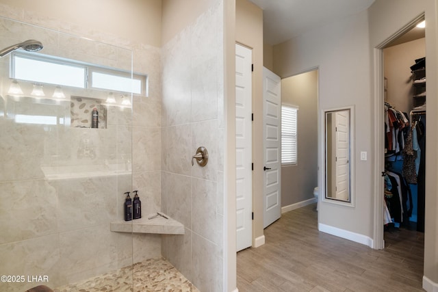 bathroom with baseboards, a spacious closet, toilet, tiled shower, and wood finished floors