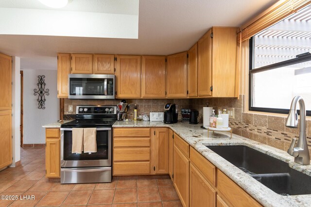 kitchen with light stone counters, light tile patterned floors, tasteful backsplash, appliances with stainless steel finishes, and a sink