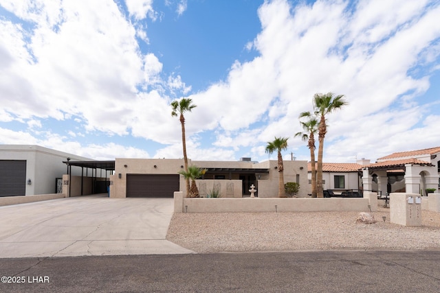 pueblo revival-style home with an attached garage, concrete driveway, and stucco siding