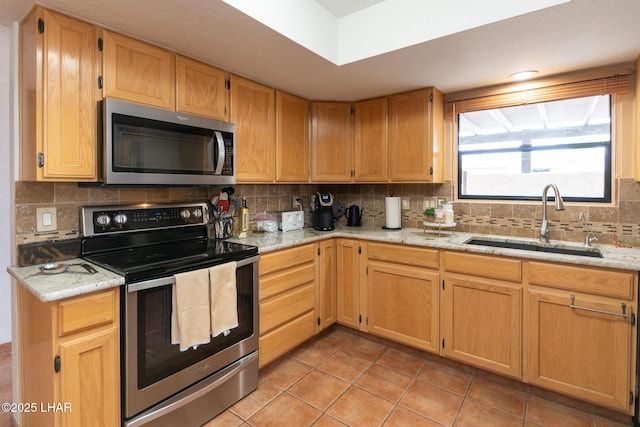 kitchen with appliances with stainless steel finishes, light tile patterned floors, a sink, and tasteful backsplash