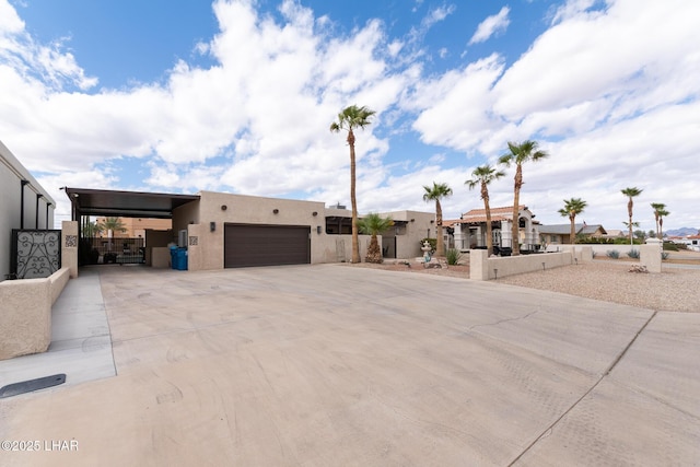 pueblo revival-style home featuring a carport, stucco siding, fence, a garage, and driveway