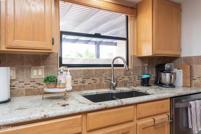 kitchen with stainless steel dishwasher, a sink, light stone countertops, and decorative backsplash