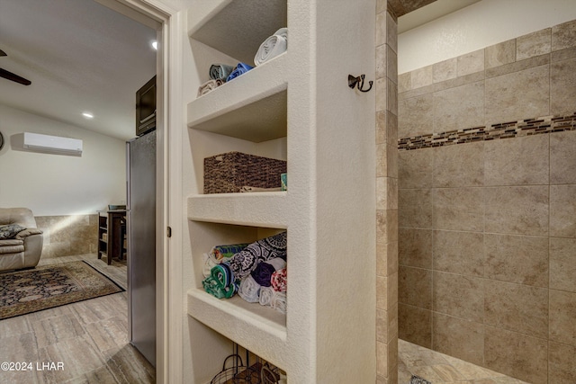 bathroom with wood-type flooring, a wall mounted AC, vaulted ceiling, and a tile shower