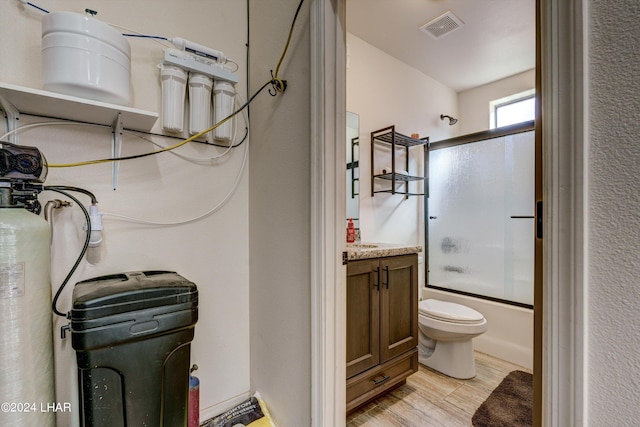 full bathroom with vanity, hardwood / wood-style floors, bath / shower combo with glass door, and toilet