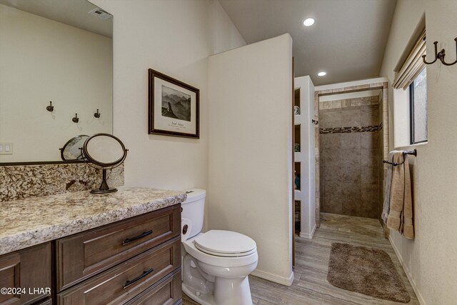 bathroom featuring hardwood / wood-style flooring, vanity, a tile shower, and toilet