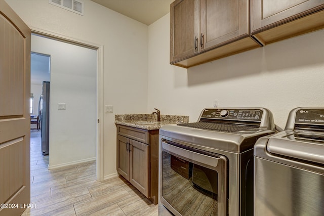 clothes washing area featuring washer and dryer, sink, and cabinets