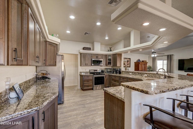 kitchen with a kitchen bar, sink, kitchen peninsula, stainless steel appliances, and light stone countertops