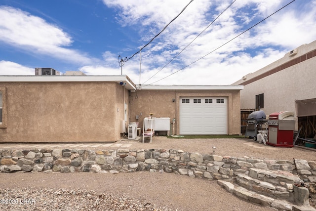 rear view of property with an attached garage, stucco siding, and dirt driveway