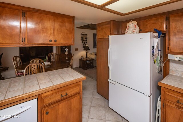 kitchen with brown cabinetry, tile countertops, freestanding refrigerator, and light tile patterned floors
