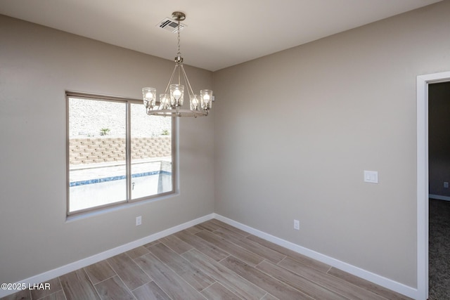 spare room featuring an inviting chandelier, wood finished floors, visible vents, and baseboards