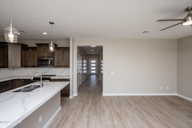 kitchen featuring a ceiling fan, appliances with stainless steel finishes, light wood finished floors, and a sink