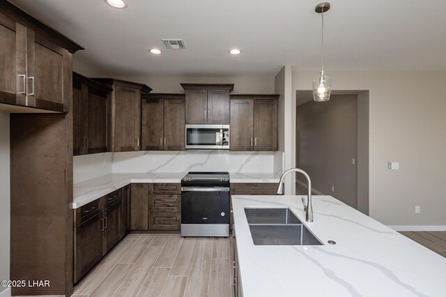 kitchen featuring stainless steel appliances, light wood-style floors, a sink, visible vents, and pendant lighting