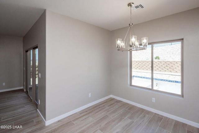 empty room with an inviting chandelier, baseboards, wood finished floors, and visible vents