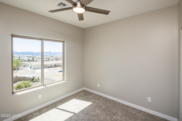spare room featuring a mountain view, a ceiling fan, visible vents, carpet, and baseboards