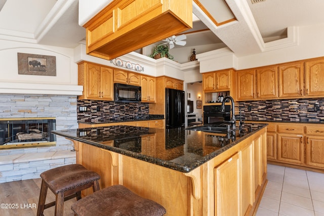 kitchen with a ceiling fan, a breakfast bar area, dark stone countertops, black appliances, and a sink