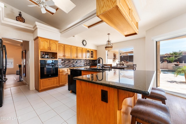 kitchen featuring light tile patterned floors, glass insert cabinets, black appliances, an island with sink, and a kitchen bar