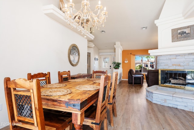 dining area with lofted ceiling, a stone fireplace, light wood-style flooring, and visible vents