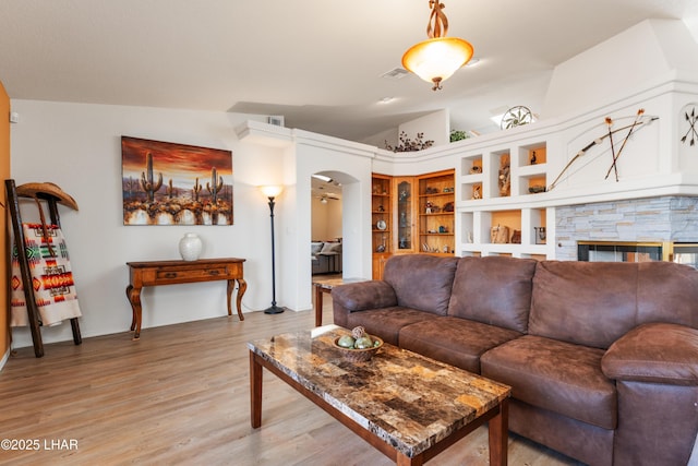 living area with arched walkways, lofted ceiling, a stone fireplace, visible vents, and light wood-style floors