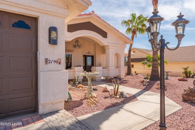 doorway to property featuring a garage, a tile roof, and stucco siding