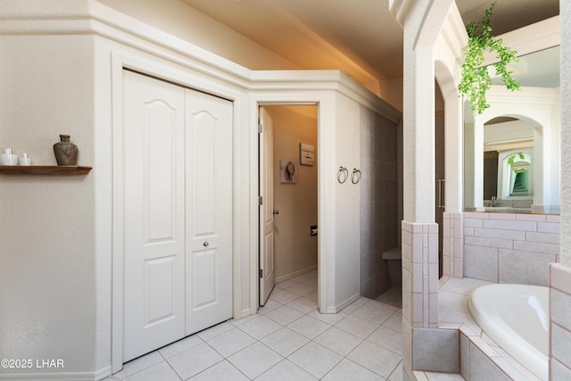 bathroom with a closet, baseboards, a bath, and tile patterned floors