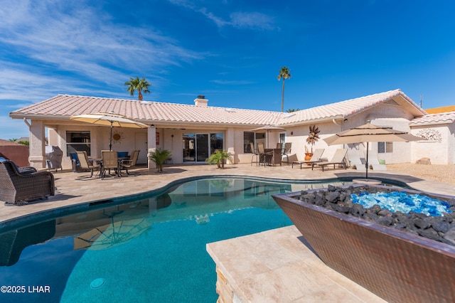 rear view of property with a patio area, a tile roof, a chimney, and an outdoor pool