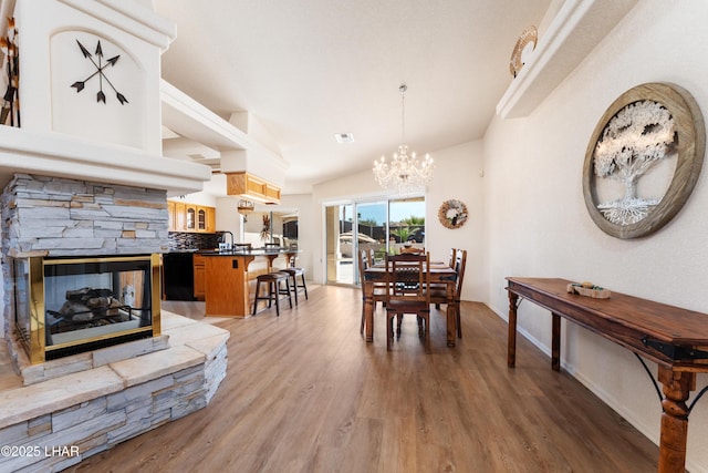 dining room featuring visible vents, a stone fireplace, a chandelier, light wood-type flooring, and baseboards