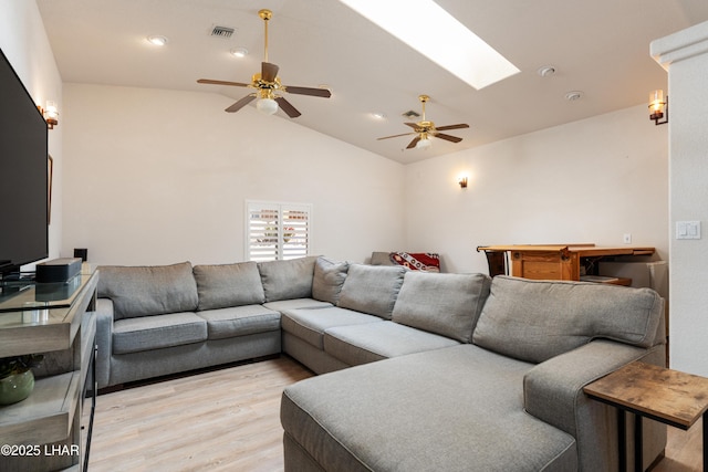 living area featuring a ceiling fan, vaulted ceiling with skylight, visible vents, and light wood finished floors