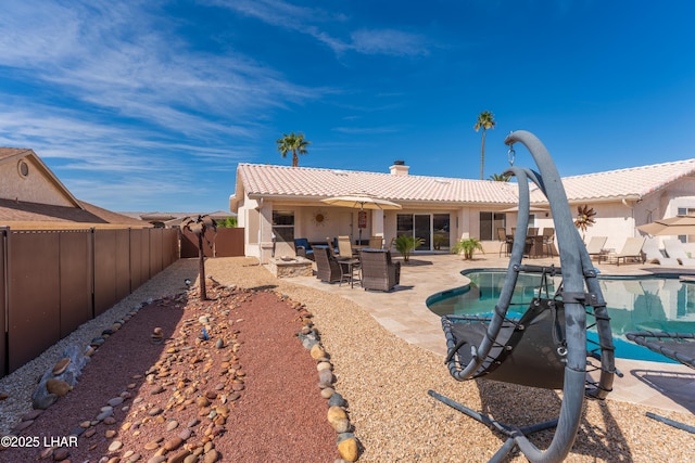 rear view of house featuring a fenced in pool, a patio, a chimney, stucco siding, and a tiled roof