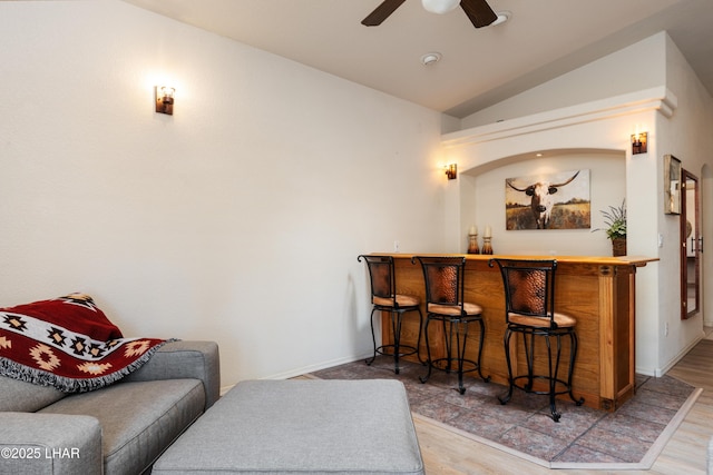 bar featuring baseboards, a ceiling fan, lofted ceiling, wood finished floors, and a bar