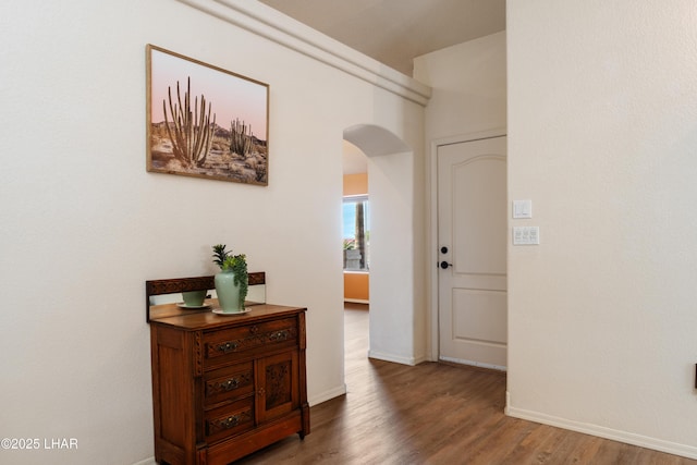 corridor featuring arched walkways, wood finished floors, and baseboards