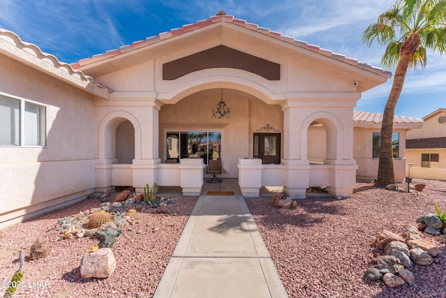 view of exterior entry featuring a tile roof, a porch, and stucco siding