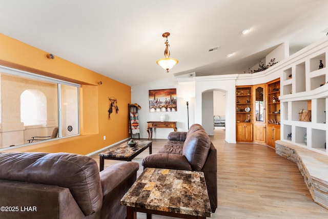 living area with arched walkways, light wood-type flooring, lofted ceiling, and visible vents