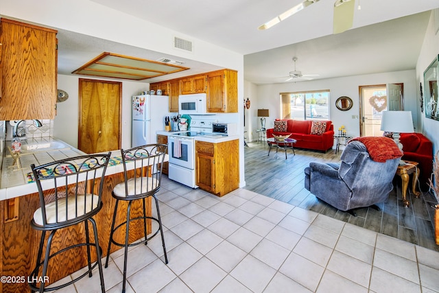 kitchen with sink, white appliances, ceiling fan, a kitchen breakfast bar, and light tile patterned flooring