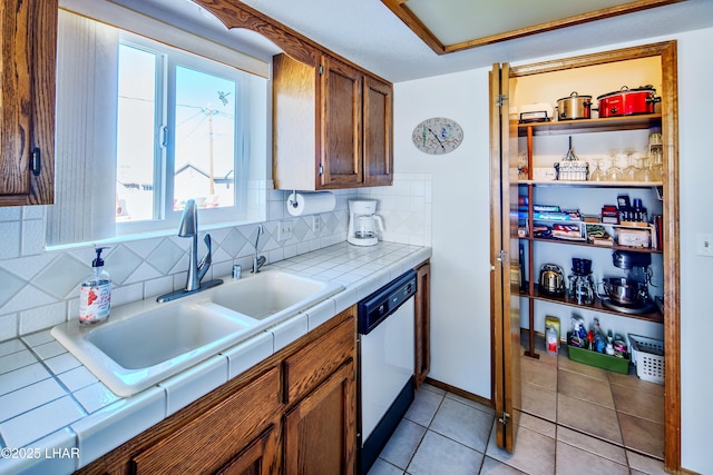 kitchen with stainless steel dishwasher, tile counters, sink, and backsplash