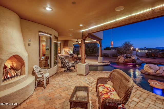 view of patio with a warm lit fireplace and a fenced in pool