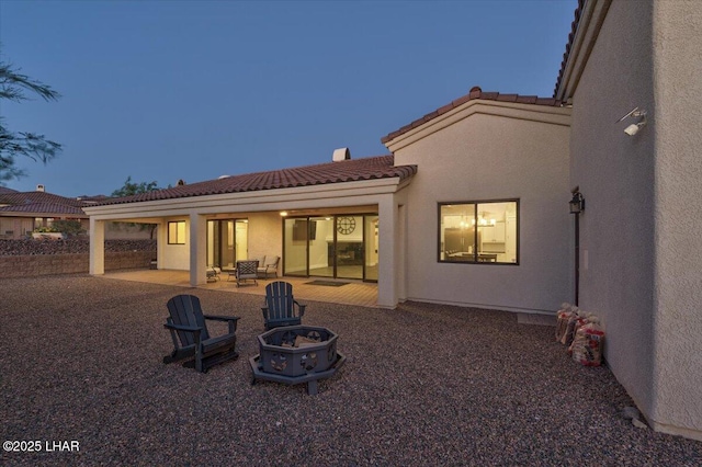 rear view of house with stucco siding, a tile roof, a patio, and an outdoor fire pit