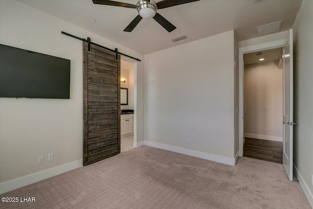 unfurnished bedroom featuring visible vents, connected bathroom, light colored carpet, and a barn door