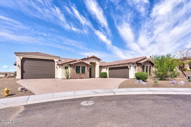 mediterranean / spanish-style house featuring a tile roof, stone siding, an attached garage, stucco siding, and decorative driveway