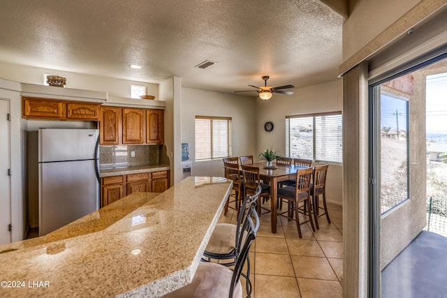 kitchen with light tile patterned flooring, a breakfast bar area, a textured ceiling, stainless steel fridge, and decorative backsplash